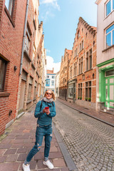 Wall Mural - Woman tourist lost in the streets of the city and is looking on his phone how to get further, Bruges, Belgium