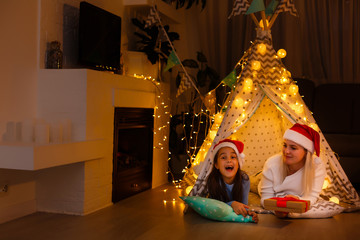 Wall Mural - mother and daughter in santa claus hats near the fireplace