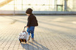Little smiling traveler girl pulls funny fluffy suitcase with rabbit to the airport.