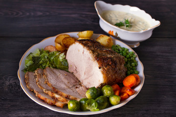 Wall Mural - Roasted sliced ham and vegetables: potatoes, carrots, brussel sprouts, cabbage and green peas on black wooden background