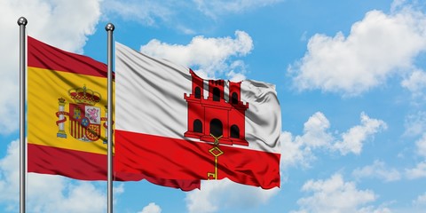 Spain and Gibraltar flag waving in the wind against white cloudy blue sky together. Diplomacy concept, international relations.