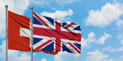 Switzerland and United Kingdom flag waving in the wind against white cloudy blue sky together. Diplomacy concept, international relations.