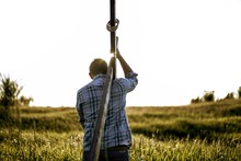 Male Carrying A Hand Made Wooden Cross In A Grassy Field Shot From Behind