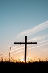 Wall Mural - Silhouette of wooden cross in a grassy field with a blue sky in the background in a vertical shot