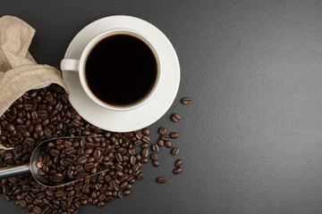 Black coffee in a white coffee cup And roasted coffee beans placed Is on the black table, the top view has space for your messages