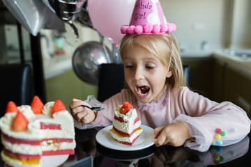 indoor shot of pretty joyful little girl with blonde hair blowing out the candle, celebrate 6 years 