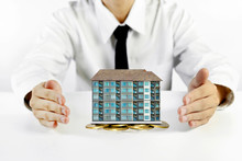 Businessman Hands Protecting Condominium Model With Piles Of Golden Coins