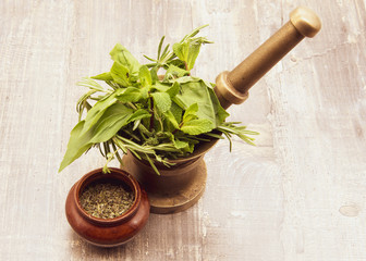 Mortar with fresh herbs and ceramic bowl with dry seasoning. On wooden background