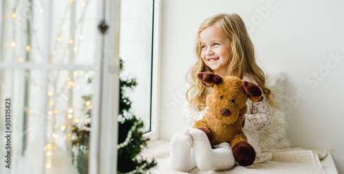 Fotomural little girl with a plush deer sitting on the window