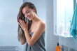 Happy attractive caucasian joyful brunette woman in bath towel applies hair conditioner in bathroom after shower at home. Hair care