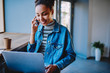 © BullRun - Cheerful hipster girl consulting with customer service about internet connection on laptop computer, happy african remote worker calling to friend via cellphone while downloading media file on netbook
