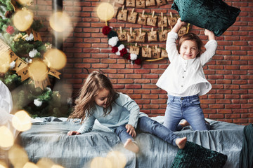 Looks like crazy pillow fight. Little girls having fun on the bed with holiday interior at the background