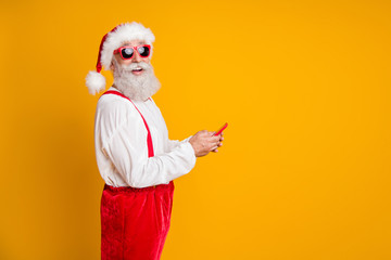 Canvas Print - Profile side photo of funky white grey hair beard santa in red hat enjoy x-mas season noel discounts greeting he search online use smartphone isolated yellow color background