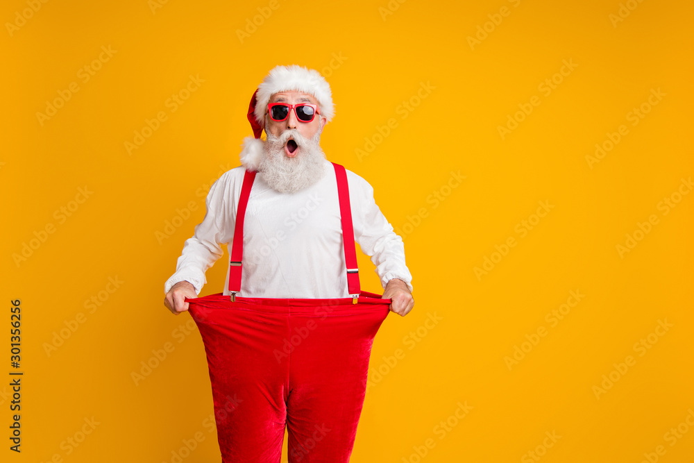 Portrait of crazy funky white bearded grandfather in santa claus hat hold big size trousers lose weight belly x-mas time show dieting effect isolated yellow color background - obrazy, fototapety, plakaty 