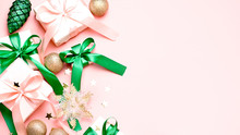 Pink Christmas Card Or New Year Background, Flat Lay, Copy Space. Pastel Pink Gift Boxes And Green, Golden Decorations And Ornaments Border On Pink Desk, Top View. Christmas Shopping Concept