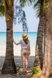 © allenkayaa - A young woman under a palm tree on the shore of the Gulf of Thailand. Woman in a hat looks at the sea