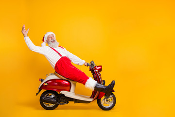 Wall Mural - Full body profile photo of funny santa white hair grandpa riding x-mas theme party by bike saying hello guests wear trousers cap shirt boots isolated yellow color background