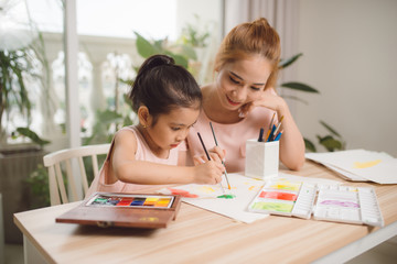 Young Asian beautiful mom with her daughter kid painting at home.