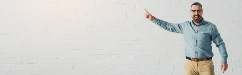 Wall Mural - panoramic shot of handsome and smiling businessman in shirt pointing with finger