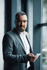 Wall Mural - handsome businessman in formal wear and glasses holding smartphone