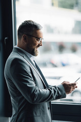 Wall Mural - handsome businessman in formal wear and glasses holding smartphone