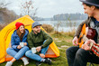 © Iryna - A group of Asian friends tourist drinking and playing guitar together with happiness in Summer while having camping near lake at sunset