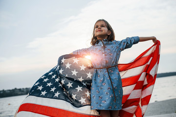 Patriotic female kid with American Flag in hands. Against cloudy sky