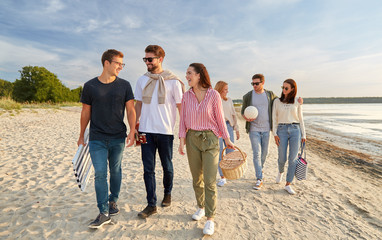 Canvas Print - friendship, leisure and people concept - group of happy friends with ball, guitar, bag and picnic basket with blanket walking along beach in summer