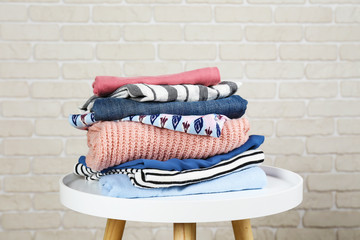 Wall Mural - Stack of clean freshly laundered, neatly folded women's clothes on wooden table. Pile of shirts, dresses and sweaters on white board, concrete wall background. Copy space, close up, top view.