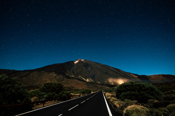 Wall Mural - Long straight asphalt black road by night with sky full of stars above - concept of travel and discover the beauty of the world - el teide vulcan national park tenerife