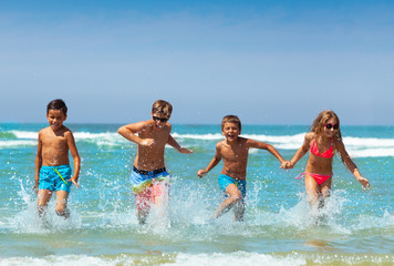 Wall Mural - Group of laughing kids run splashing in the sea