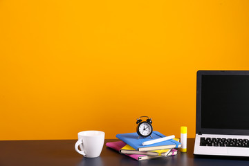 Wall Mural - Blank screen laptop computer, various supplies on wooden desk over bright yellow wall background with a lot of copy space for text. Creative workspace. Close up shot of table w/ computer & stationery.