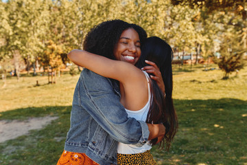 Wall Mural - Two happy affectionate diverse young women friends hugging each other in the park - two friends hugging each other outdoors 