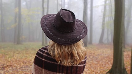 Wall Mural - woman with hat wrapped in blanket is looking to fog. moody atmosphere in misty forest at autumn. dou
