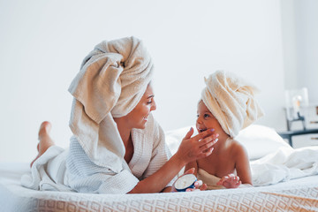 Using cream. Young mother with her daugher have beauty day indoors in white room