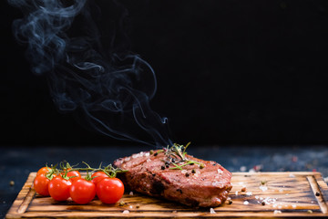 Steakhouse menu. Rib eye steak. Closeup of grilled beef meat with cherry tomatoes and burning rosemary twig. Copy space.