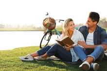 Happy Young Couple Reading Book While Having Picnic Outdoors