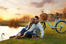 Young Couple Near Lake With Swan At Sunset. Perfect Place For Picnic