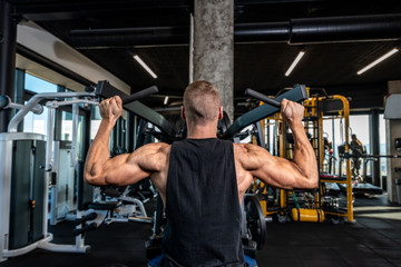 Young strong muscular sweaty fit bodybuilder man back muscles workout training in the gym on the machine