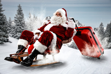 Wall Mural - Red Santa Claus riding a wooden sled. An older man with a beard delivers presents to a child. Winter mountains landscape and snow-covered trees with frost. Fir branches, winter time. Christmas spells