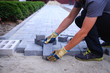 © Ivan Kmit - The master in yellow gloves lays paving stones in layers. Garden brick pathway paving by professional paver worker. Laying gray concrete paving slabs in house courtyard on sand foundation base.