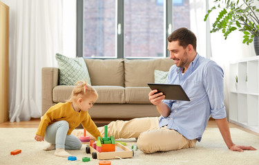 Wall Mural - family, fatherhood and people concept - happy father with tablet pc computer and little baby daughter playing with wooden toy toy blocks kit at home