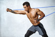 © Romario Ien - Man performs exercises with expander. Photo of sporty man workout on grey background. Strength and motivation