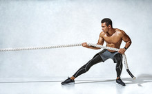 Strong Man Pulling Rope. Photo Of Sporty Man On Grey Background. Strength And Motivation. Side View. Full Length