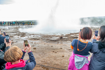 Poster - GEYSIR, ICELAND - JULY 30, 2019: Tourists enjoy Geysir geyser eruption on a cloudy afternoon