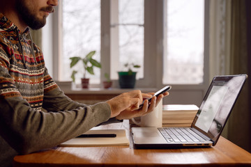 Freelancer is making actions in smartphone while working at home.