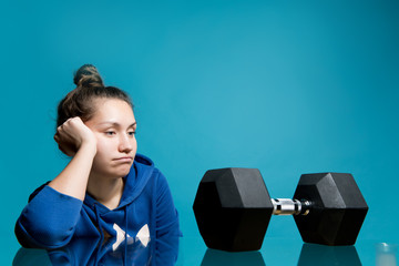 the girl looks in frustration and longing at the big dumbbell lying in front of her