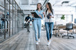 © Roman - Sharing fresh office news. Two young colleagues in smart casual wear discussing business and smiling while walking through the office