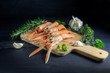 Fresh scampi, also called Norway Lobster or langoustine on a kitchen board, also garlic and herbs, ingredients for an festive seafood meal on a dark gray wooden background
