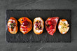 Mixed crostini appetizers with a variety of toppings. Top view on a dark slate background. Party food concept.